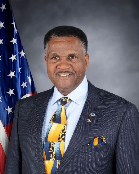 Commissioner Clifton Dollison smiling in front of an American Flag.